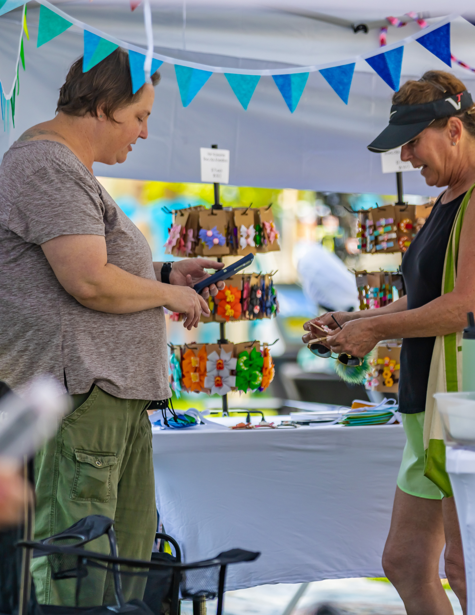 Woman purchasing an item from a vendor booth at the Berthoud Market, with handmade goods on display.